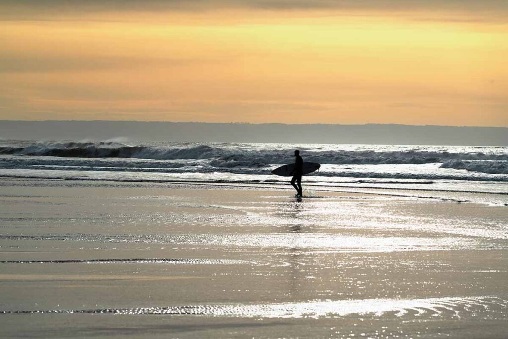 Surfer leaving the water at Croyde Bay, sun setting